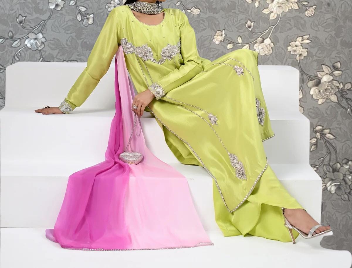 A woman wearing a bright green dress with pink accents is sitting on a white step. She is holding a small purse in her hand.