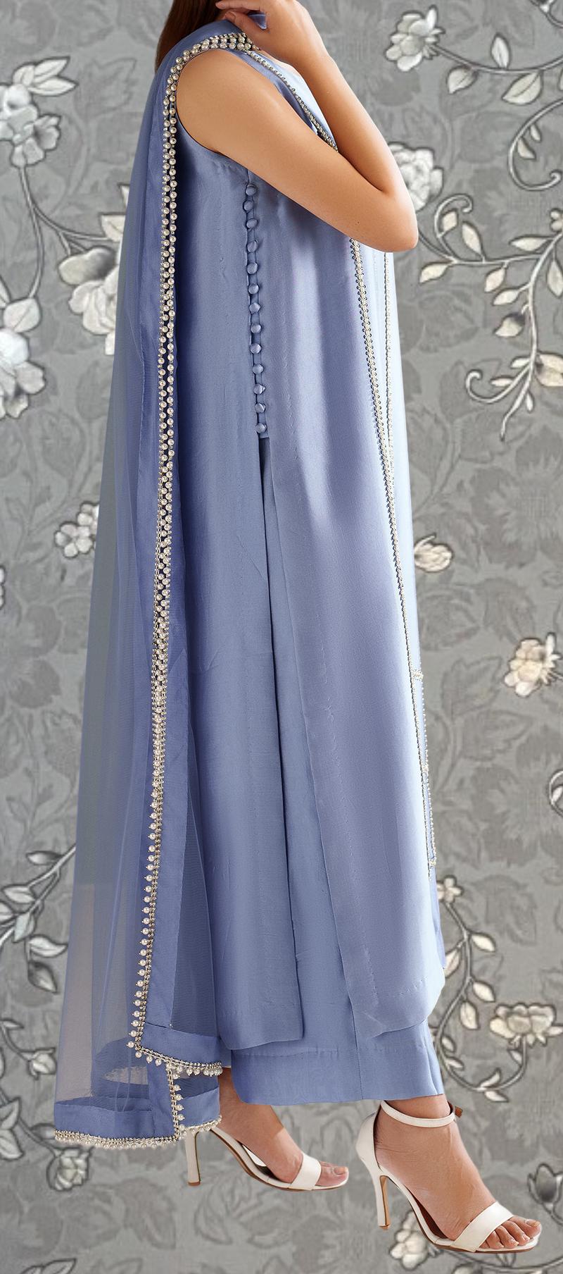 A woman wearing a long, sleeveless blue dress with a sheer overlay and beaded trim, paired with white high heels.