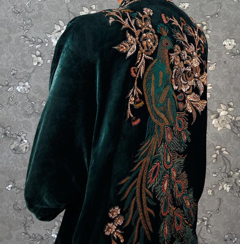 a close-up view of a dark green velvet jacket with intricate gold and green embroidered designs, including a peacock feather and flowers.