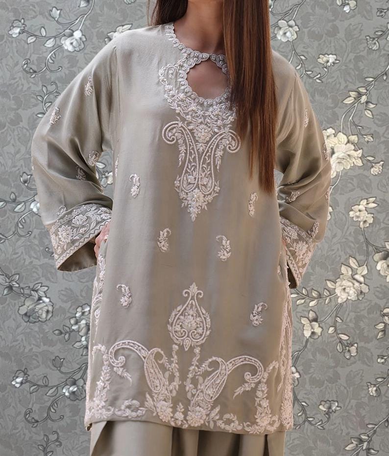A woman wearing a grey dress with intricate embroidered patterns on the front.