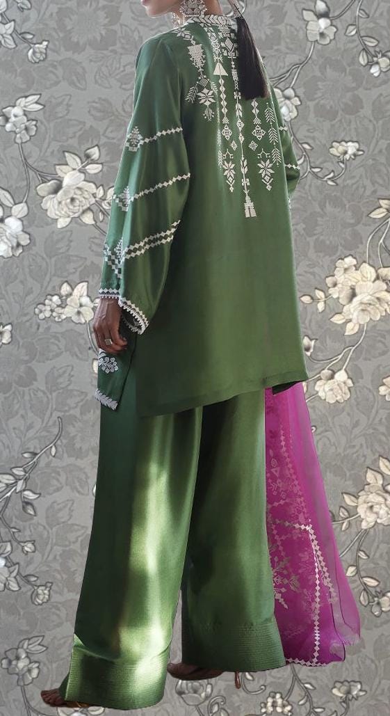 A person wearing a green outfit with white embroidered designs on the back, standing against a gray floral background.