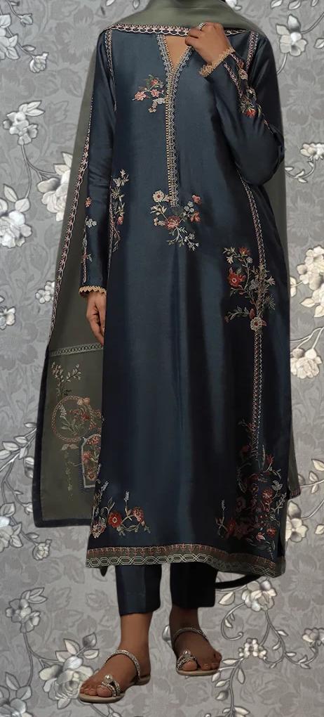 A person wearing a long, dark blue dress with intricate floral embroidery on the front and sleeves, standing against a floral patterned background.