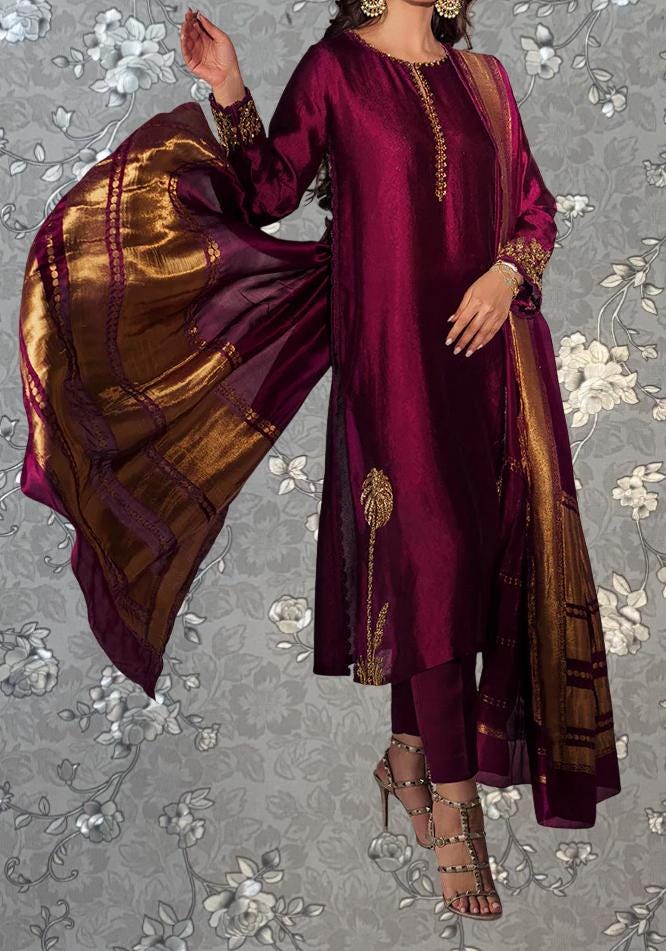 A woman wearing a long, burgundy dress with gold accents, including a matching shawl, stands against a gray floral background.