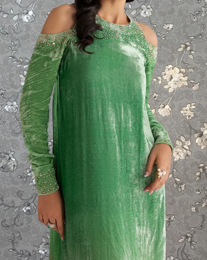 A woman wearing a long, green dress with beaded embellishments on the shoulders and neckline.