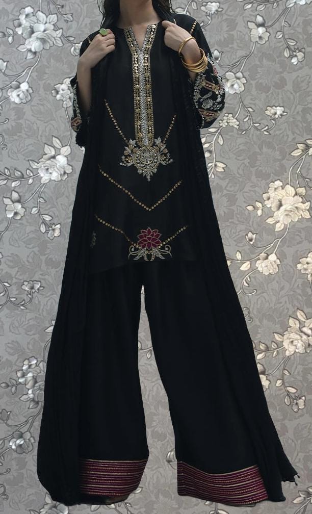 A person wearing a black dress with gold embroidery and a long black shawl.