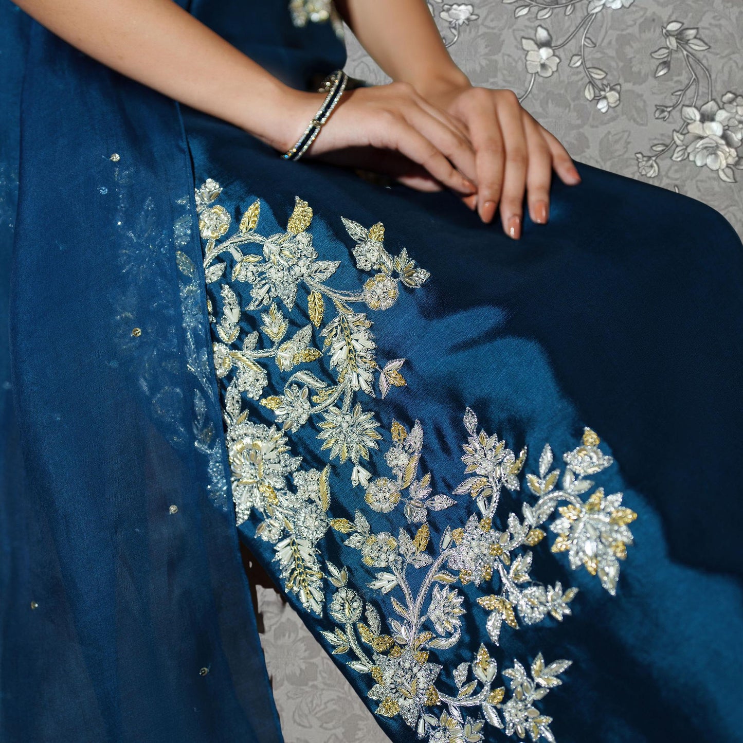 A close-up view of a woman's hand wearing a blue dress with intricate gold embroidery.