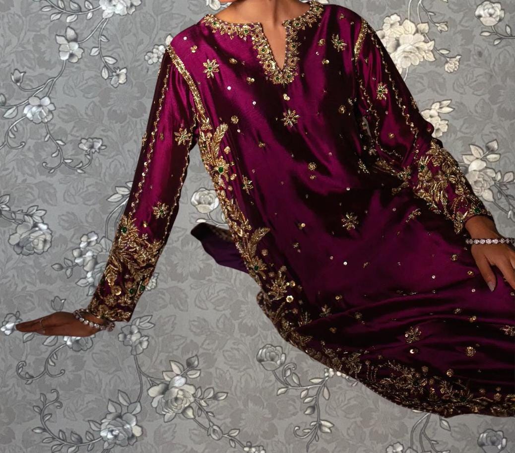 A close-up of a person wearing a long, purple dress with gold embroidery and a high neckline.