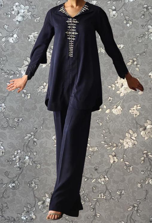 A person wearing a navy blue dress with a floral pattern and a high collar, standing against a gray floral background.