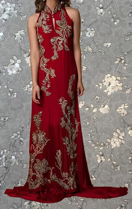 A woman wearing a long, red dress with intricate gold embroidery stands against a gray floral background.