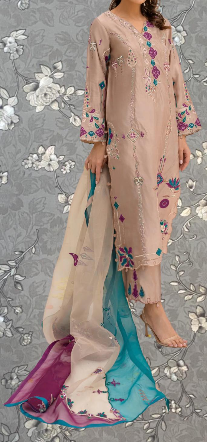 A woman wearing a long, light pink dress with intricate embroidered designs in shades of purple and blue, standing against a gray floral background.