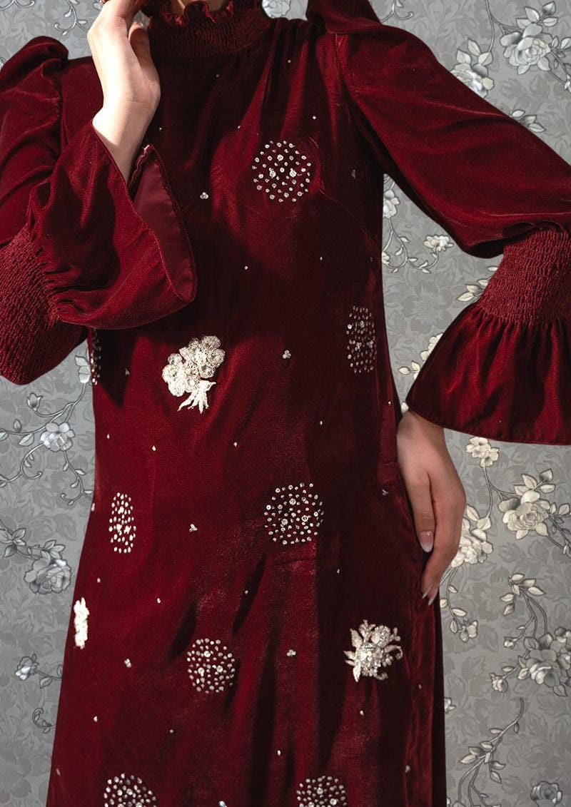 A close-up of a person wearing a red dress with white polka dots, posing against a floral background.