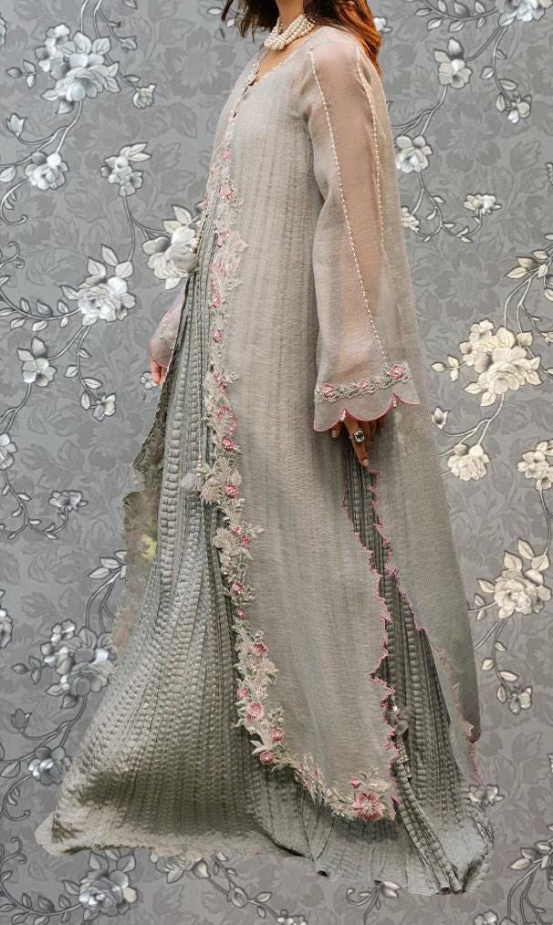 A woman wearing a long, flowing gray dress with intricate floral embroidery and a sheer overlay.
