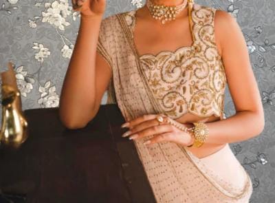 A woman wearing a gold and white dress with intricate embroidery poses elegantly against a gray floral background.