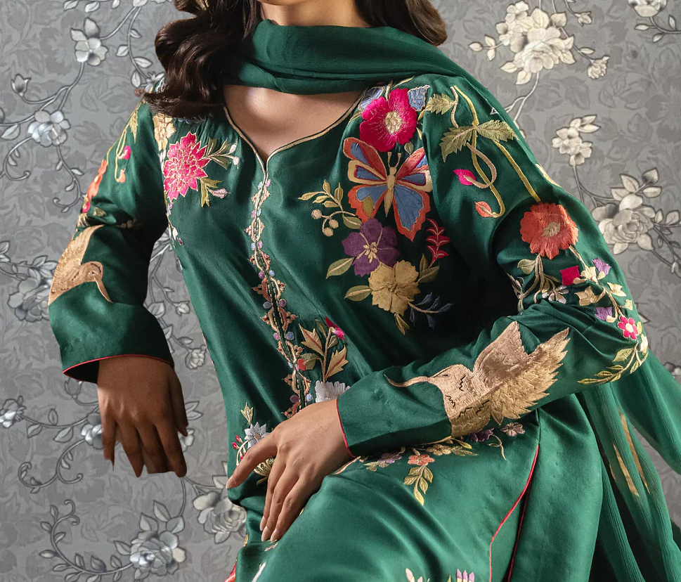 A close-up of a woman wearing a green dress with intricate embroidered designs, including flowers and birds.