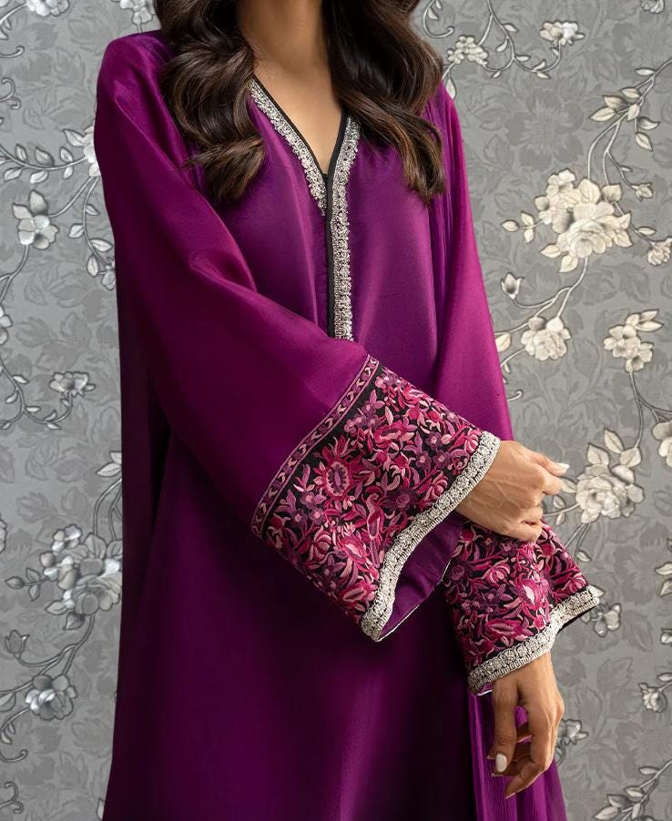 A woman wearing a long purple dress with intricate floral embroidery on the sleeves and collar.