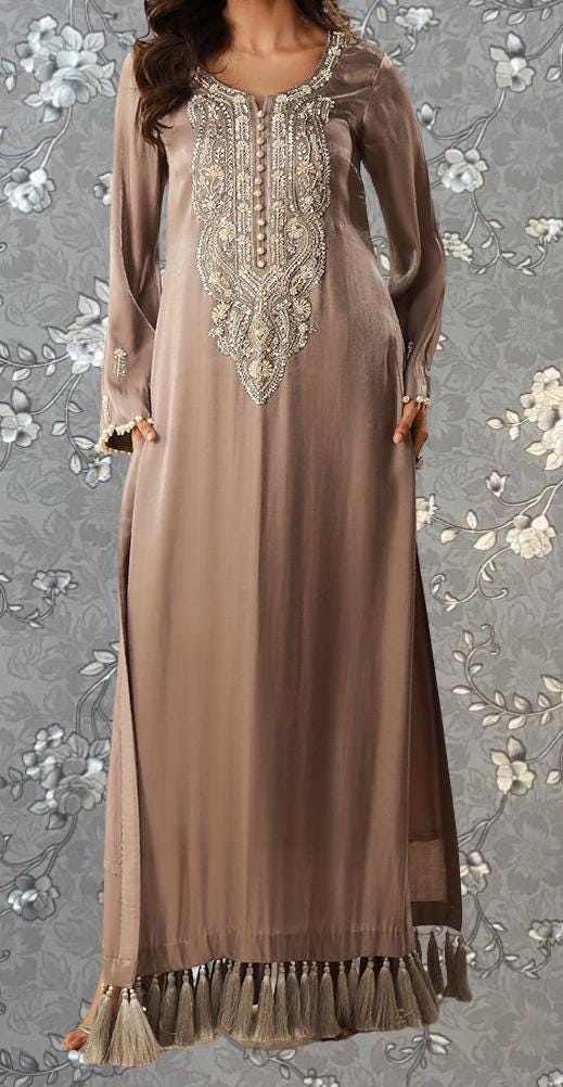 A woman wearing a long, beige dress with intricate embroidery and tassels on the bottom.