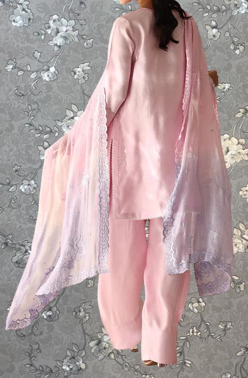 A woman wearing a pink dress with a matching pink shawl, standing against a gray floral background.
