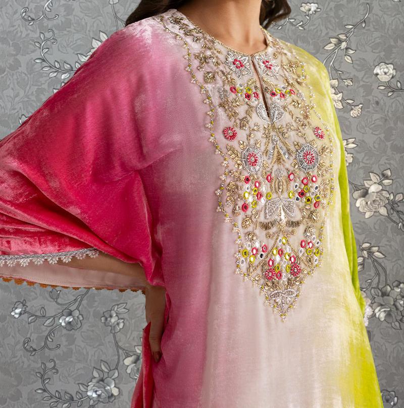 A close-up of a woman wearing a colorful, intricately embroidered dress with a pink and yellow gradient.