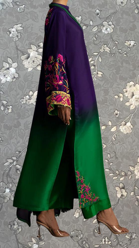 A person wearing a long, colorful dress with floral embroidery on the sleeves and a green and purple gradient.