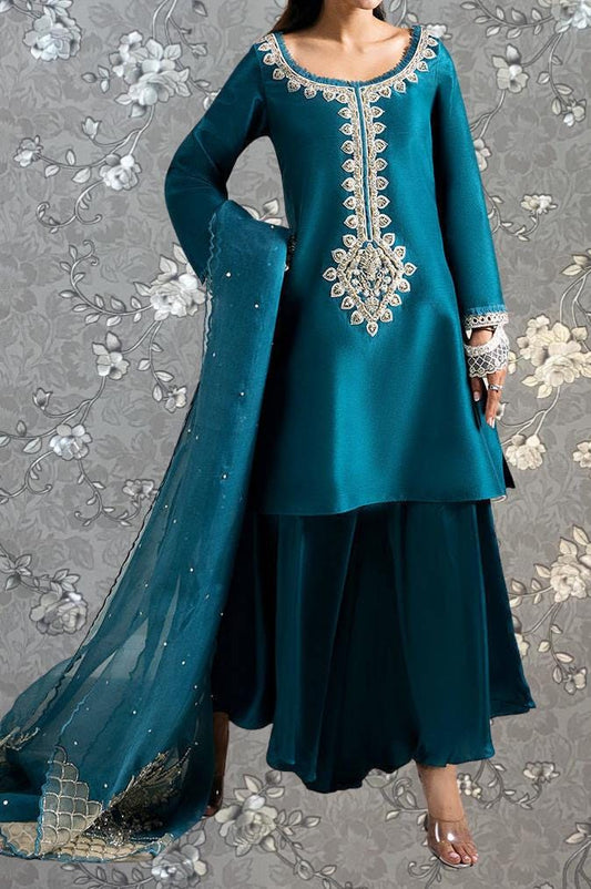 A woman wearing a teal blue dress with intricate embroidery and a matching shawl.