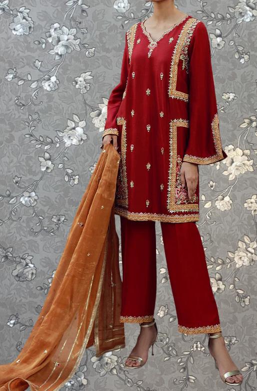 A woman wearing a red and gold traditional outfit with a matching shawl, standing against a gray floral background.
