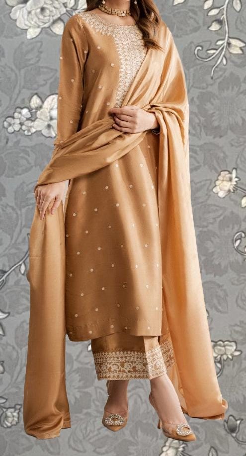 A woman wearing a gold and beige dress with a matching shawl, standing against a gray floral background.
