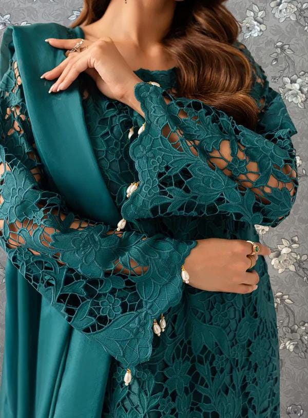 A woman wearing a teal green lace dress with intricate embroidery and a matching green shawl draped over her shoulders.