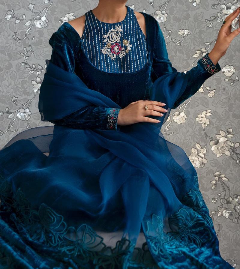 A woman wearing a blue dress with a floral pattern and a matching blue shawl is shown against a gray floral background.