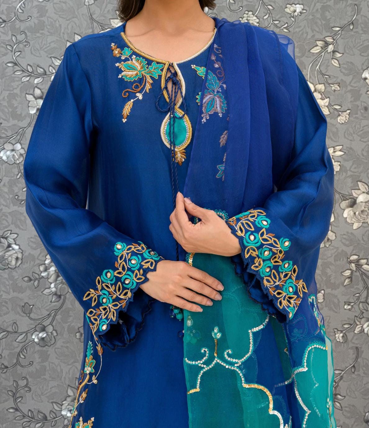 A woman wearing a blue dress with intricate embroidered designs on the sleeves and collar.