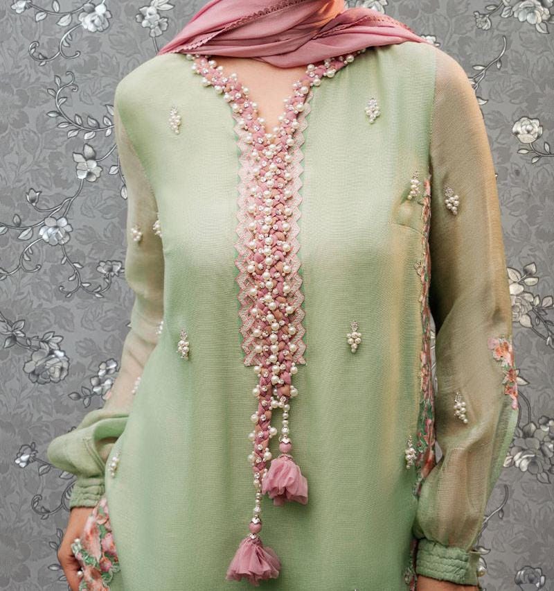 A woman wearing a green dress with pink and white embellishments, including a long beaded neckline and a tassel.