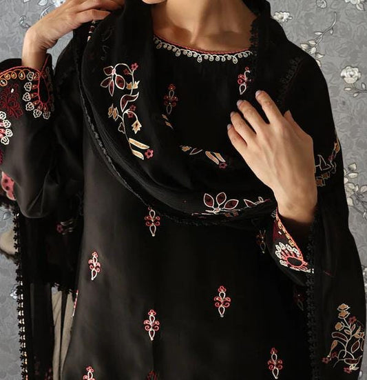 A close-up of a person wearing a black dress with intricate floral embroidery on the sleeves and collar.