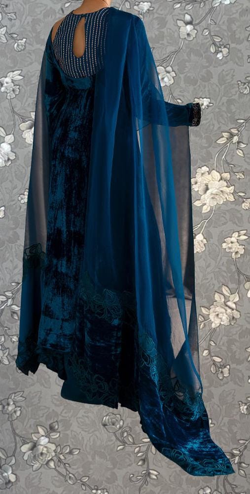 A blue velvet dress with a sheer blue cape draped over the back, set against a gray floral background.