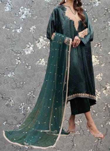 A woman wearing a long green dress with a matching green and gold shawl, standing against a gray floral background.