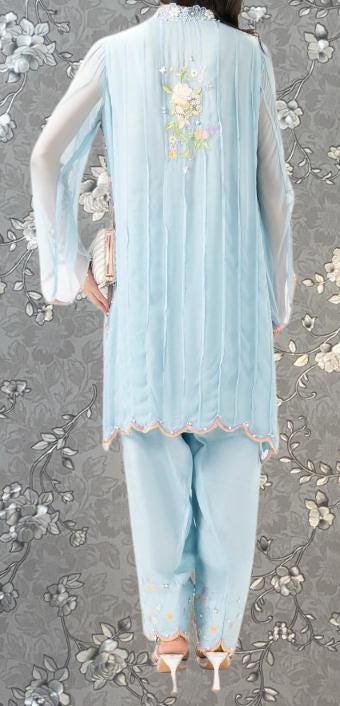 A person wearing a light blue dress with a floral pattern on the back, standing against a gray floral background.