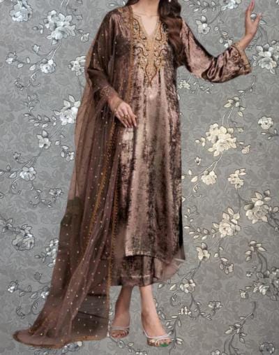 A woman wearing a long, brown dress with gold embroidery and a matching shawl stands against a gray floral background.