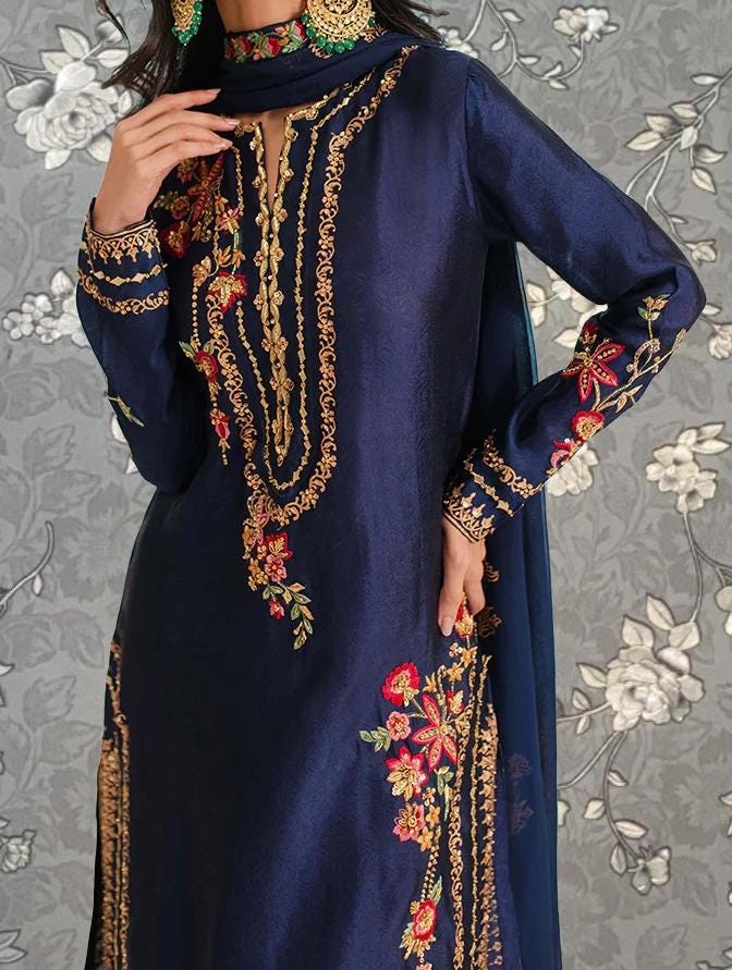 A woman wearing a navy blue dress with intricate gold embroidery and floral designs.