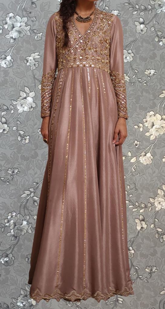 A woman wearing a long, pink dress with gold embroidery and a high neckline.
