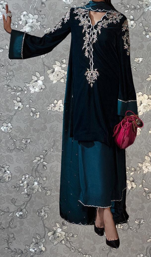 A woman wearing a long, dark blue dress with intricate embroidery and a matching purse stands against a floral patterned background.