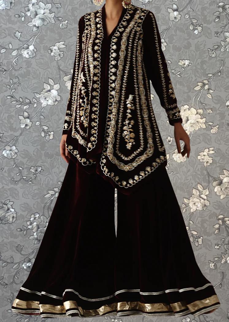 A woman wearing a long, burgundy dress with intricate gold embroidery and a matching jacket.
