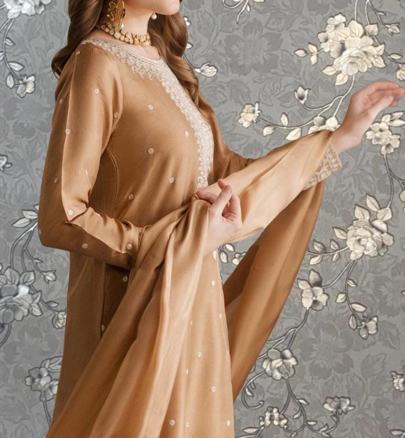 A woman wearing a gold dress with white polka dots stands in front of a gray floral wallpaper.