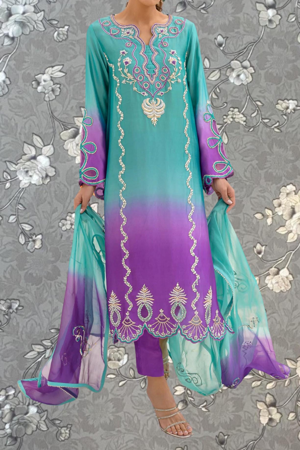 A woman wearing a long, colorful dress with intricate embroidery and patterns in shades of blue, purple, and white.