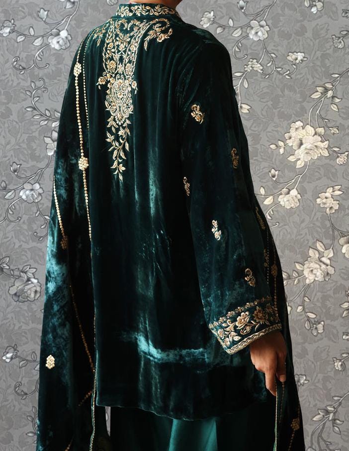 a person wearing a green velvet robe with gold embroidery, standing against a gray floral background.