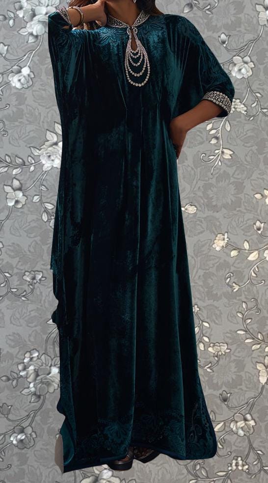 A woman wearing a long, flowing green velvet dress with a floral pattern on the background.