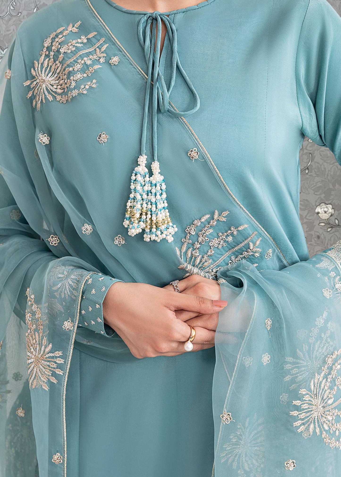 A close-up view of a person wearing a light blue dress with intricate embroidered designs and a matching light blue shawl.