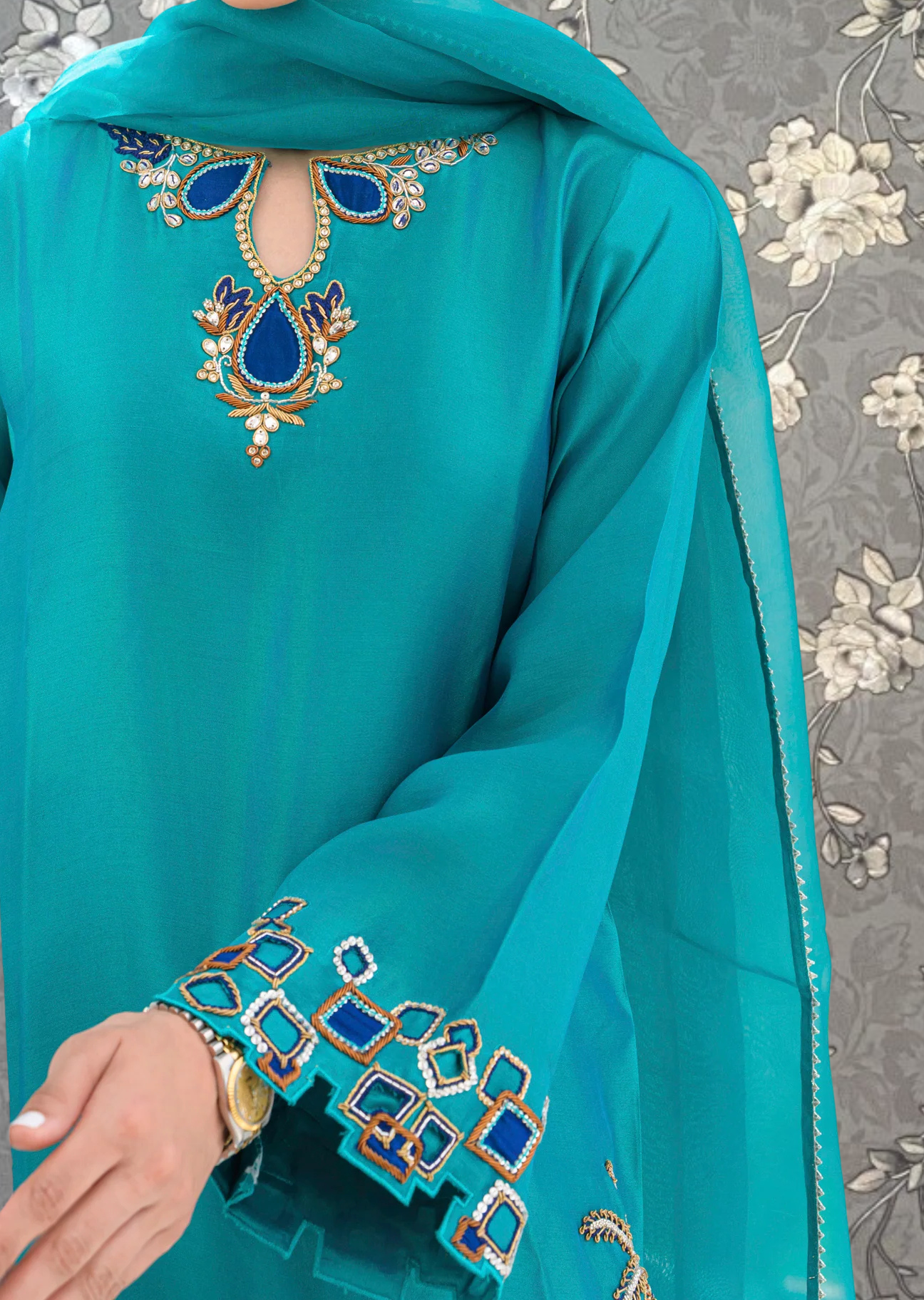 A close-up view of a person wearing a turquoise dress with intricate embroidered designs on the front.