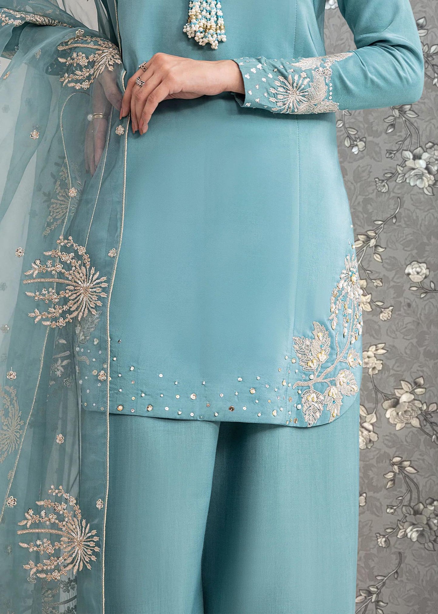 A close-up view of a person wearing a light blue dress with intricate embroidered designs on the sleeves and hem.