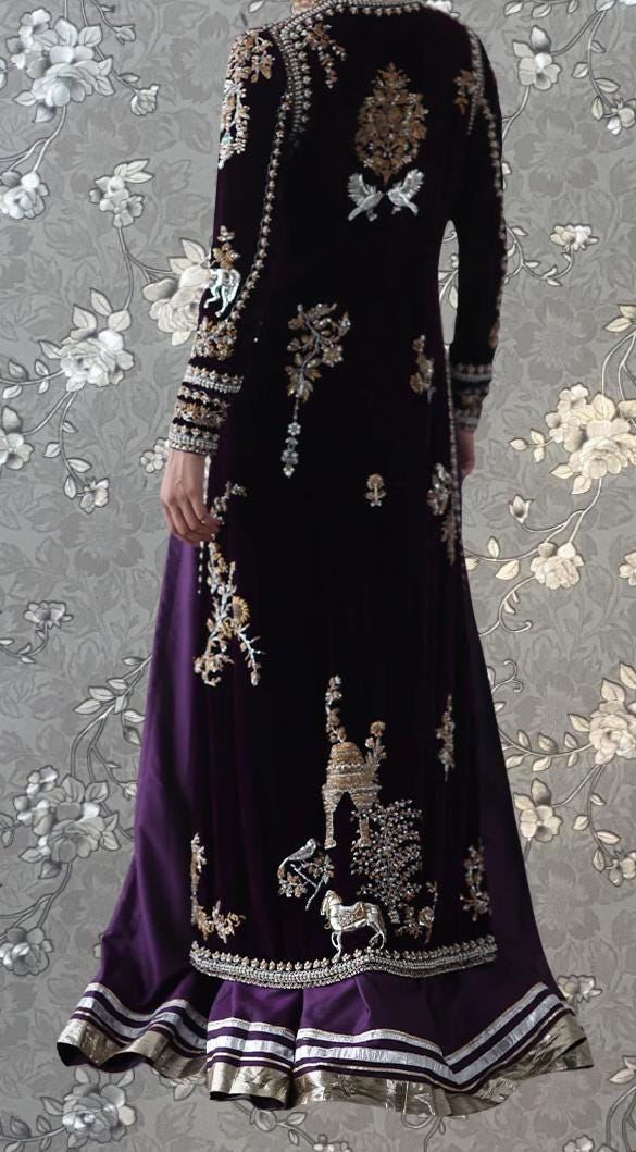 a long, purple dress with intricate gold embroidery and a matching purple skirt. The dress has a high collar and long sleeves, giving it a formal and elegant appearance.