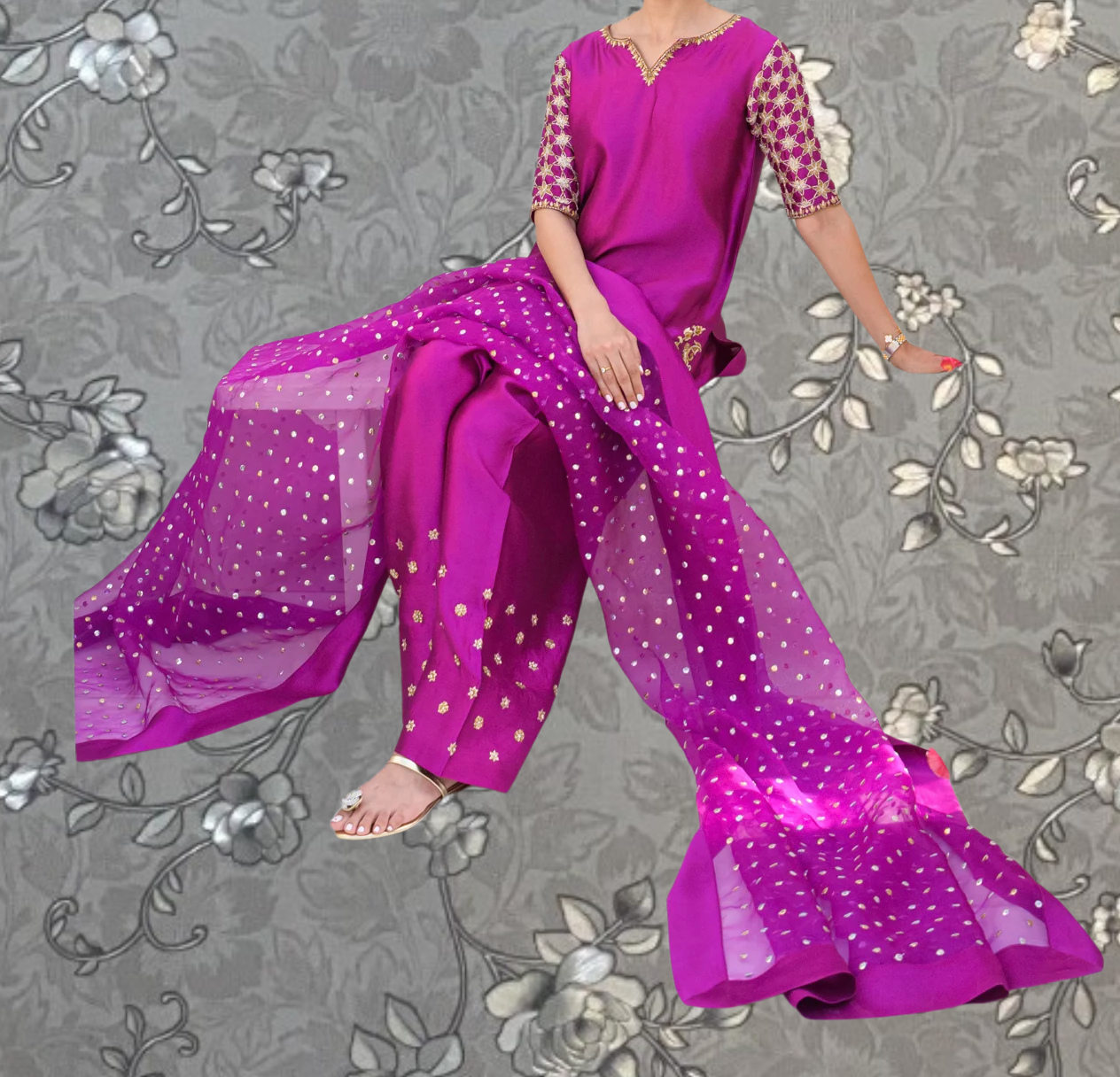 A person wearing a vibrant purple dress with polka dot accents, sitting on a floral patterned background.