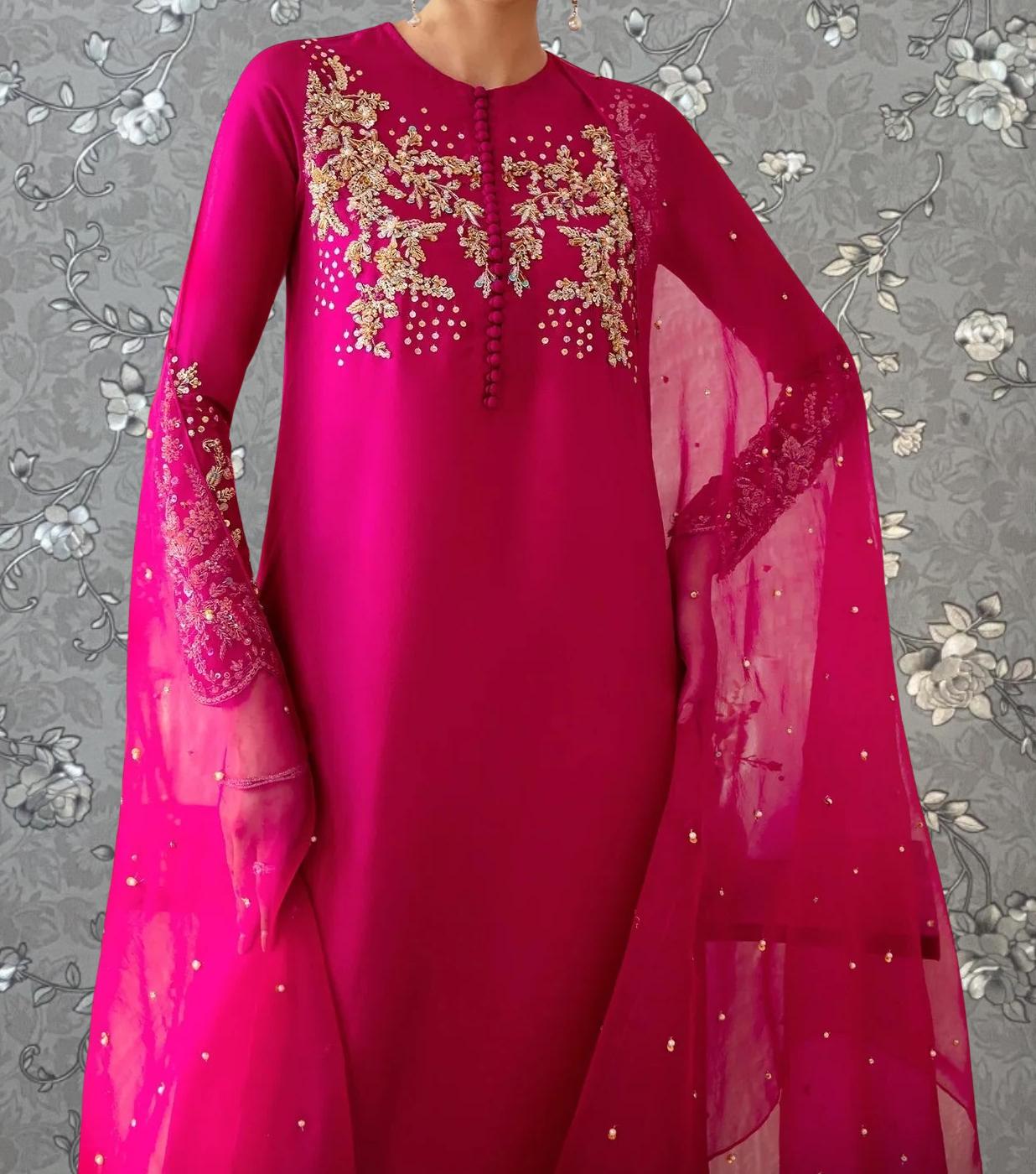 A woman wearing a long pink dress with intricate embroidered designs on the sleeves and collar.