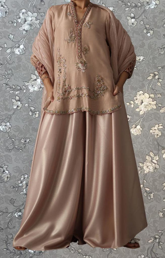 A woman wearing a long, beige dress with intricate embroidery and a matching shawl.